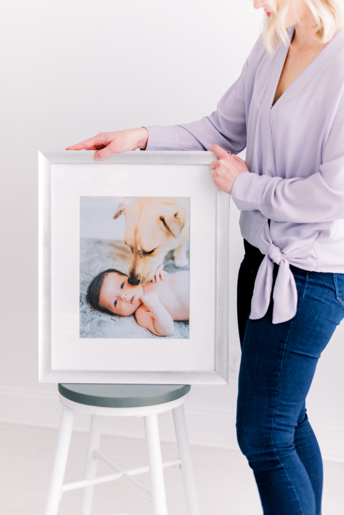 Valerie Worth (photographer) holding framed photo of newborn baby boy and dog.