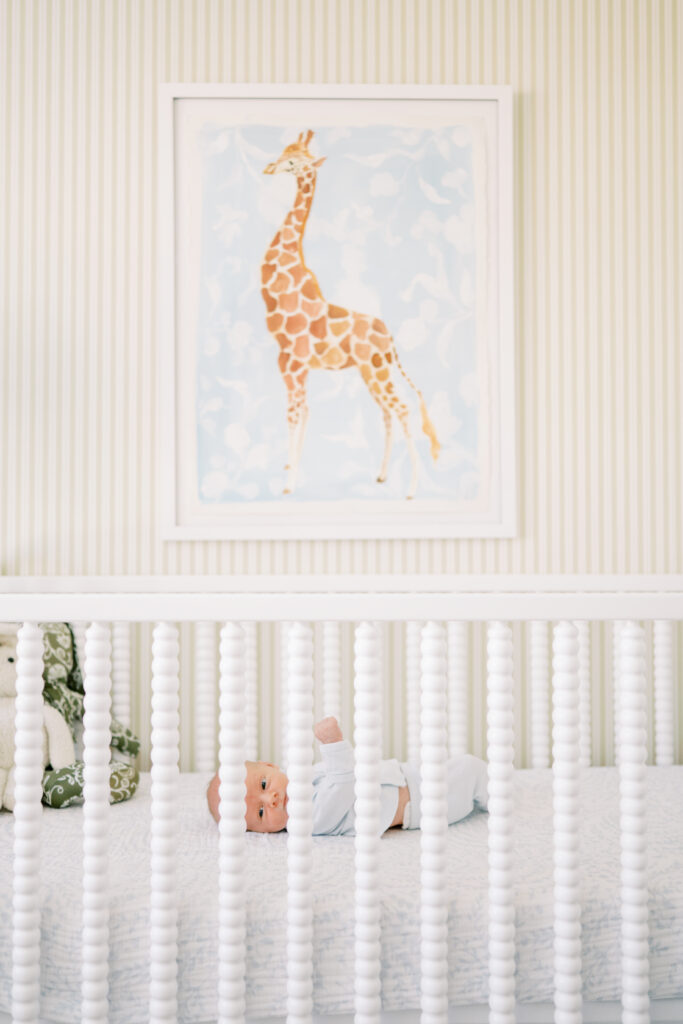 Baby boy lays in white crib in nursery with giraffe art during in-home newborn photos