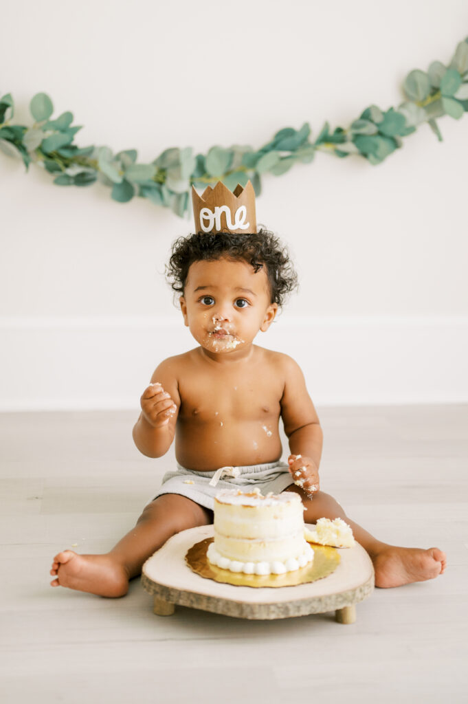 Baby boy with crown sits with birthday cake during smash cake photography session