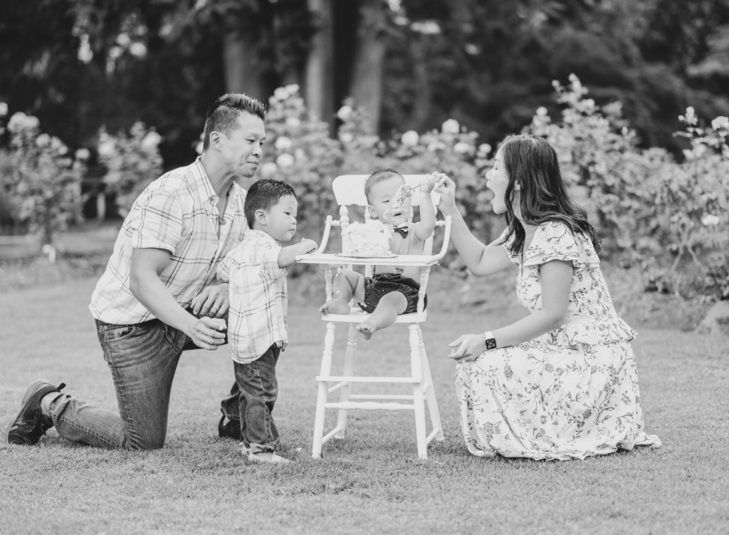 Family helps baby boy eat cake during rose garden photo session