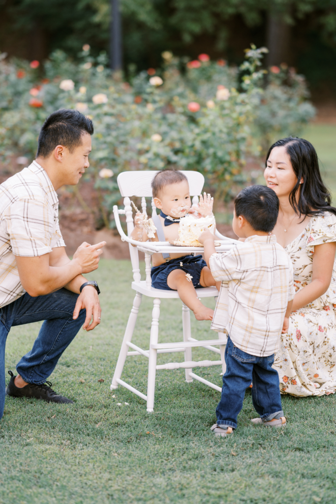 Family helps baby eat first birthday cake during photo session