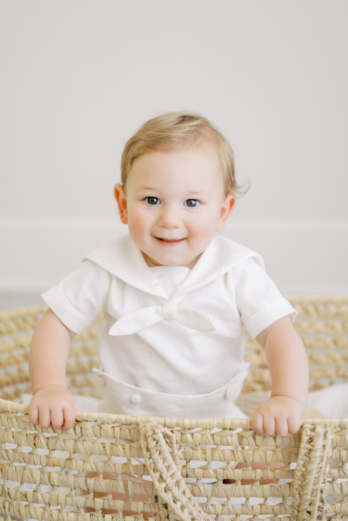 Baby boy in a white sailor romper laughing during a first birthday studio session with a Raleigh cake smash photographer.