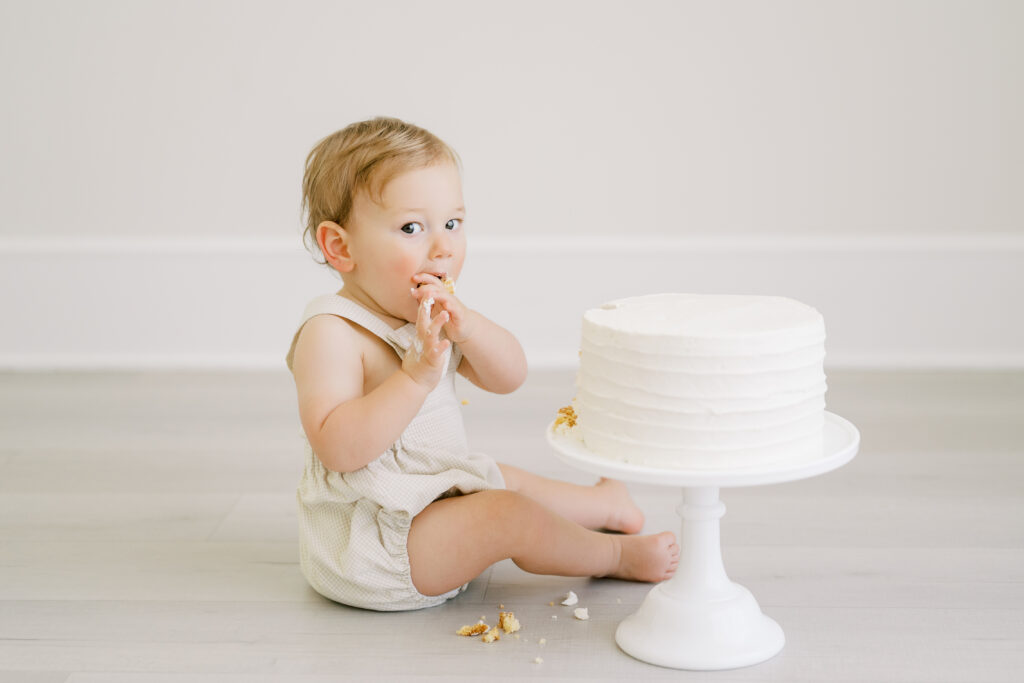 Baby boy tastes birthday cake in Raleigh photography studio during his cake smash session with Worth Capturing Photography.