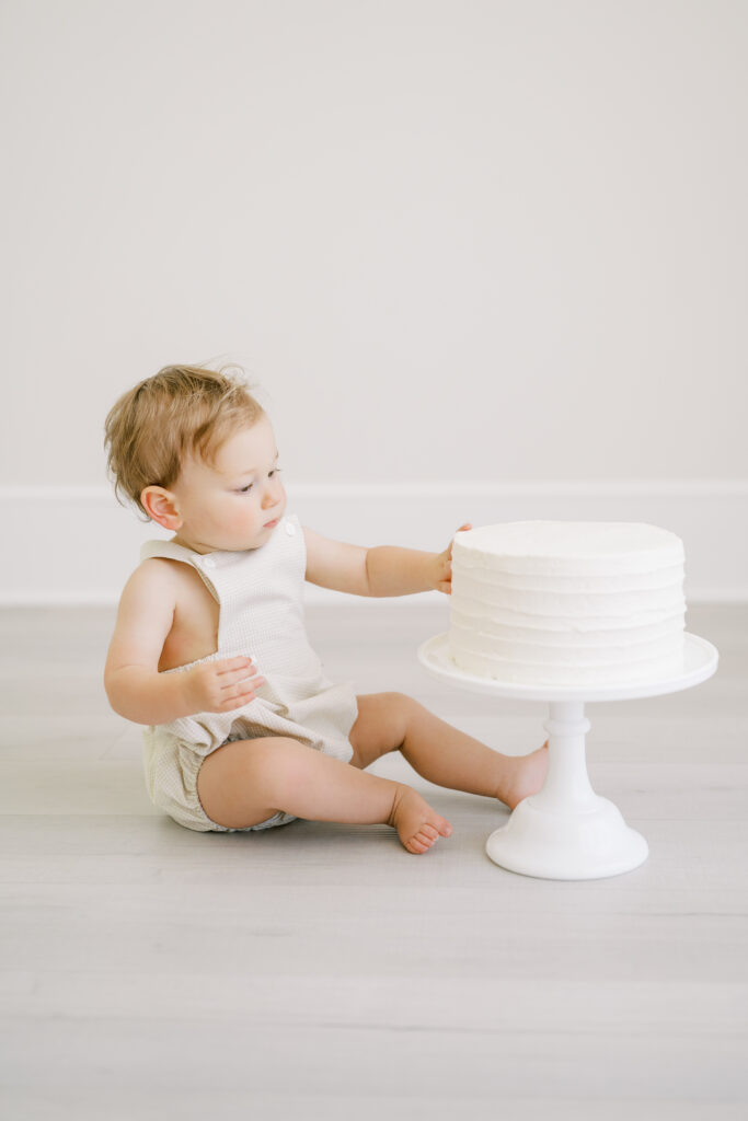 One year old boy touching frosting on cake during a studio first birthday cake smash in Raleigh, NC.