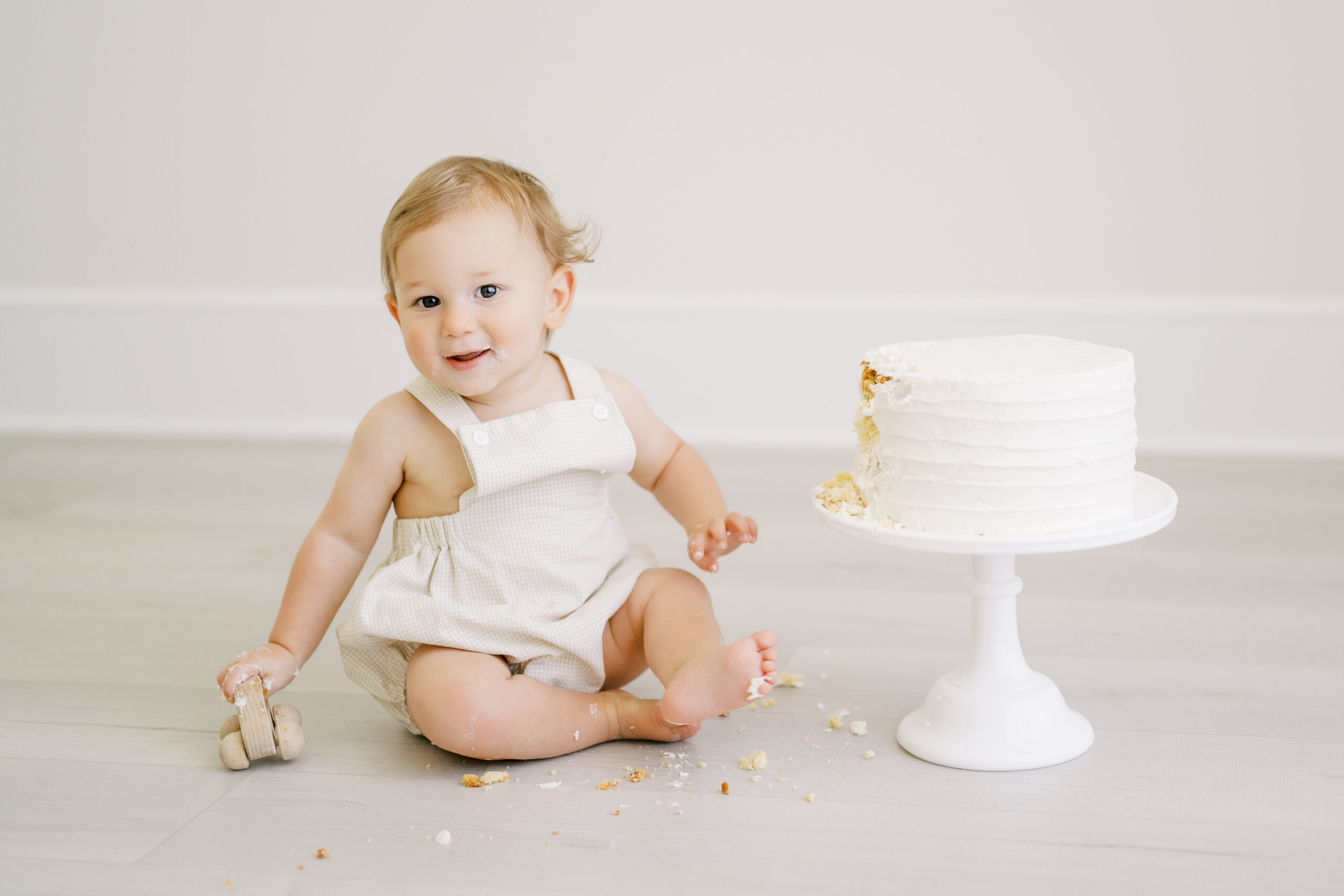 One year old boy with frosting on his face beside his first birthday cake at a Raleigh cake smash studio session.