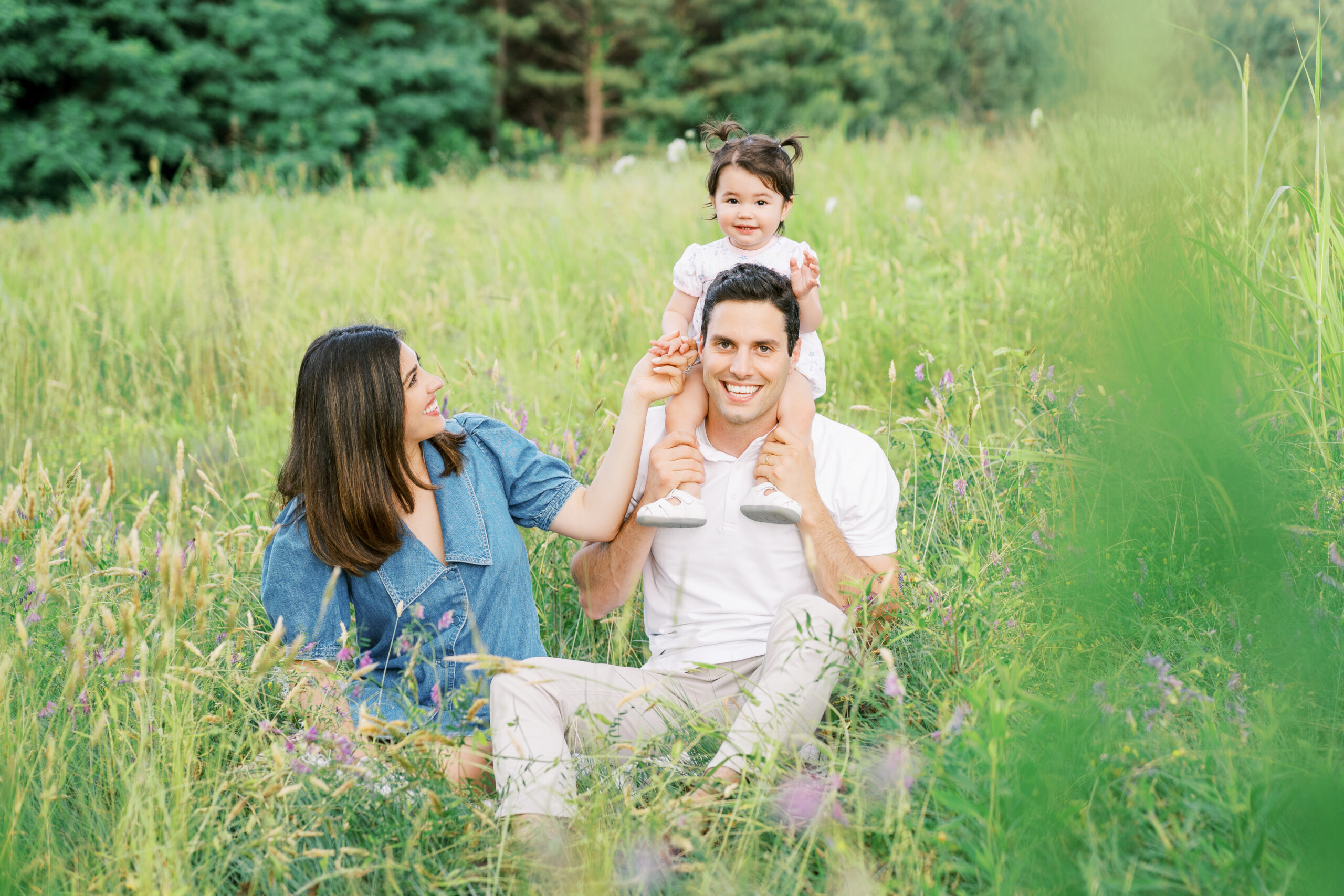 Family of three sits in green field during family photos with Raleigh family photographer at NC Museum of Art park.